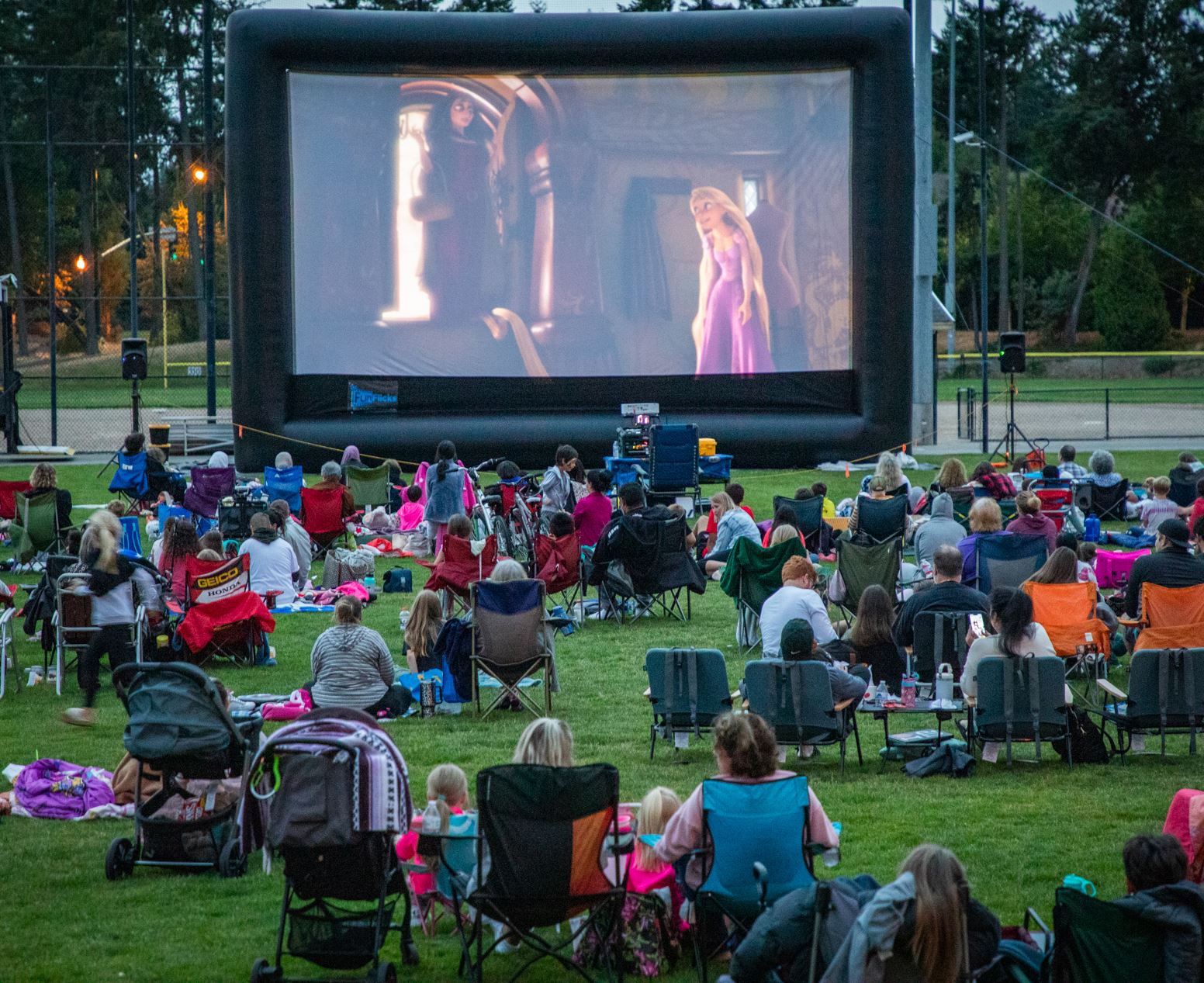 Moviegoers laid out on the ground in chairs and on blankets watching the movie on a big screen