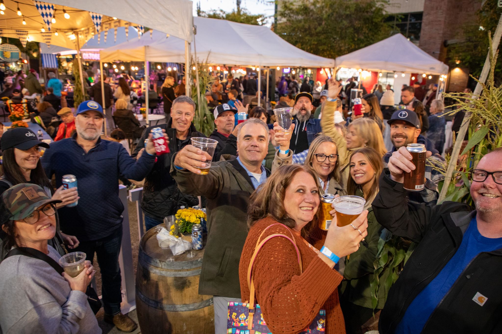 Large group of people raising beer glasses in toast, beer tents in the background
