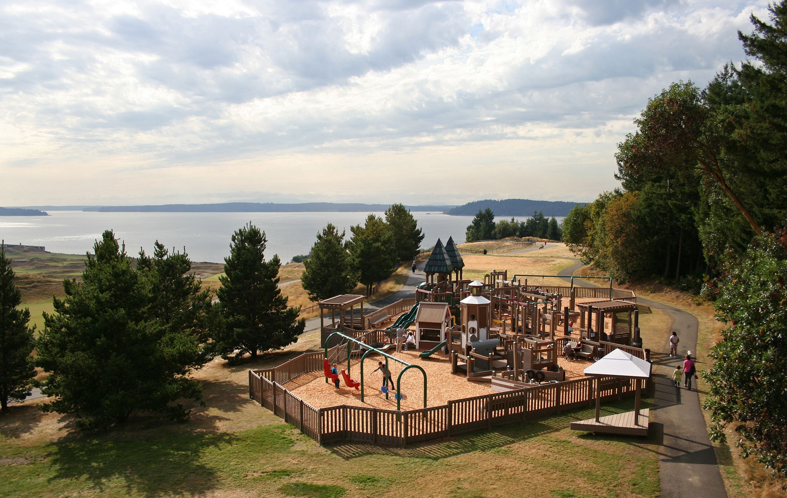 A playground sits among trees a short way from the water